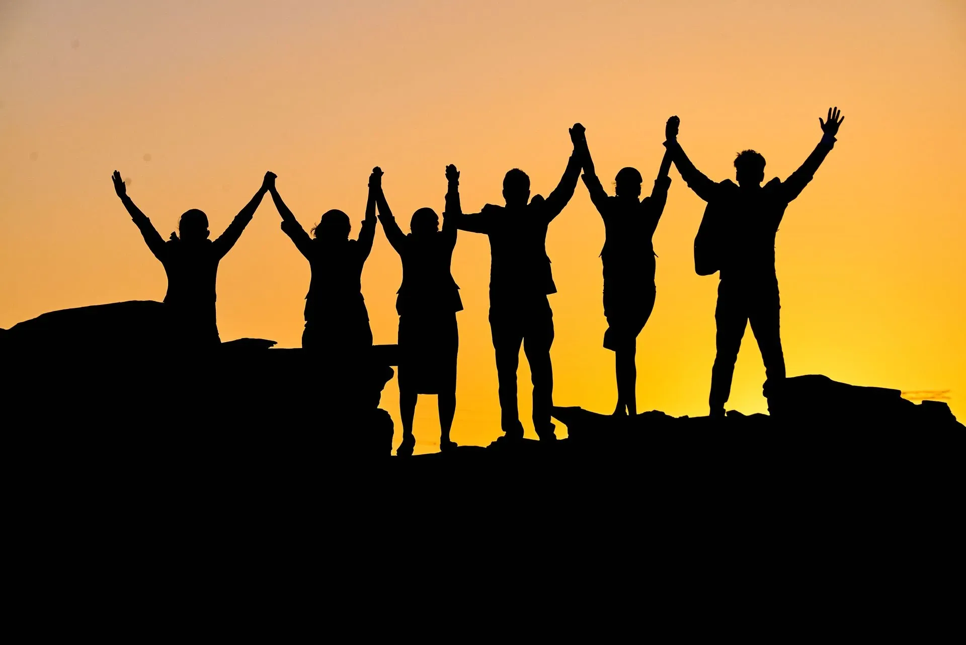 A team raising their arms on a ridge at sunrise